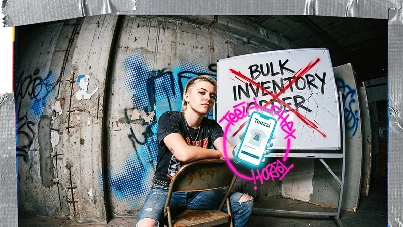 A creator sitting in front of a board with bulk inventory crossed out while holding up a phone with a merch page on screen.